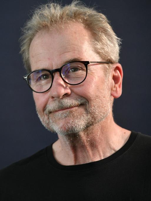 Der Regisseur Ulrich Seidl im schwarzen Hemd vor dunklem Hintergrund