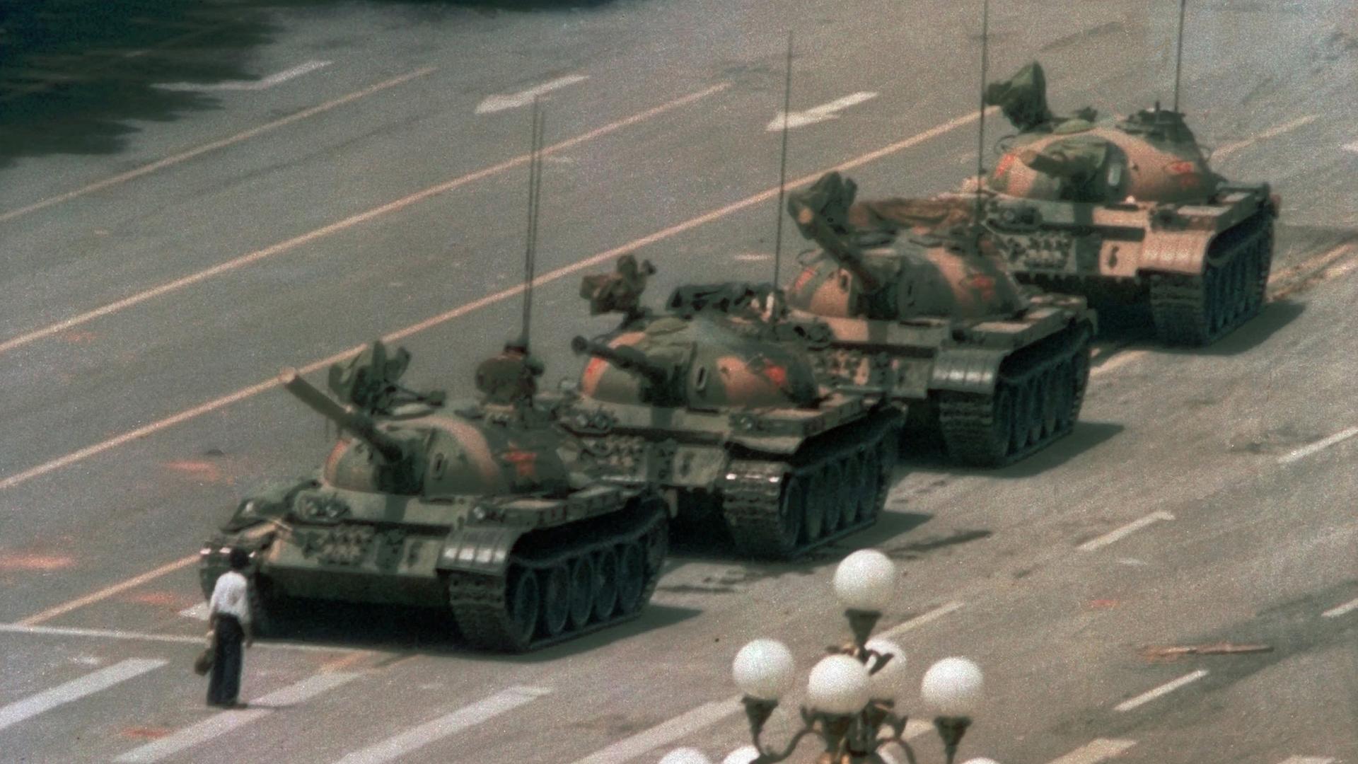 Ein chinesischer Mann steht auf einer breiten Straße vor einer Panzerkolonne, um sie aufzuhalten.