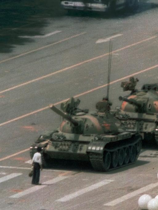 Ein chinesischer Mann steht auf einer breiten Straße vor einer Panzerkolonne, um sie aufzuhalten.