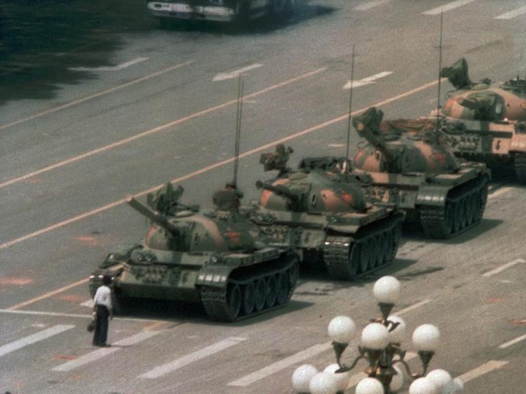 Ein chinesischer Mann steht auf einer breiten Straße vor einer Panzerkolonne, um sie aufzuhalten.