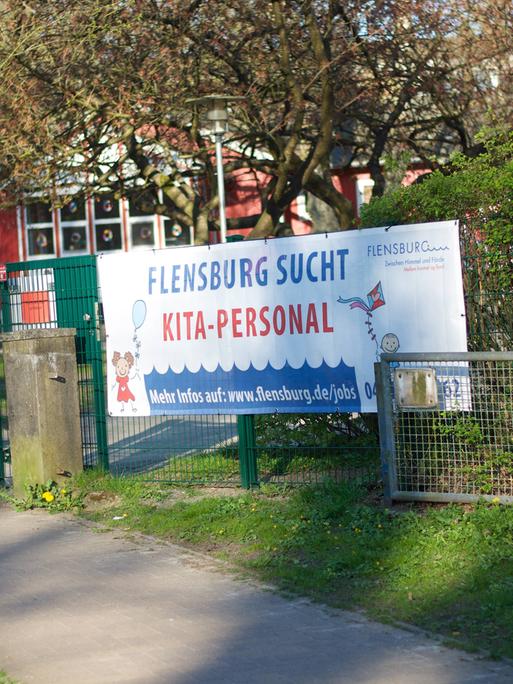 Transparent vor einer Kita mit der Aufschrift: Flensburg sucht Kita-Personal.