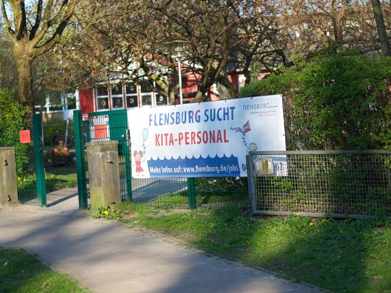 Transparent vor einer Kita mit der Aufschrift: Flensburg sucht Kita-Personal.