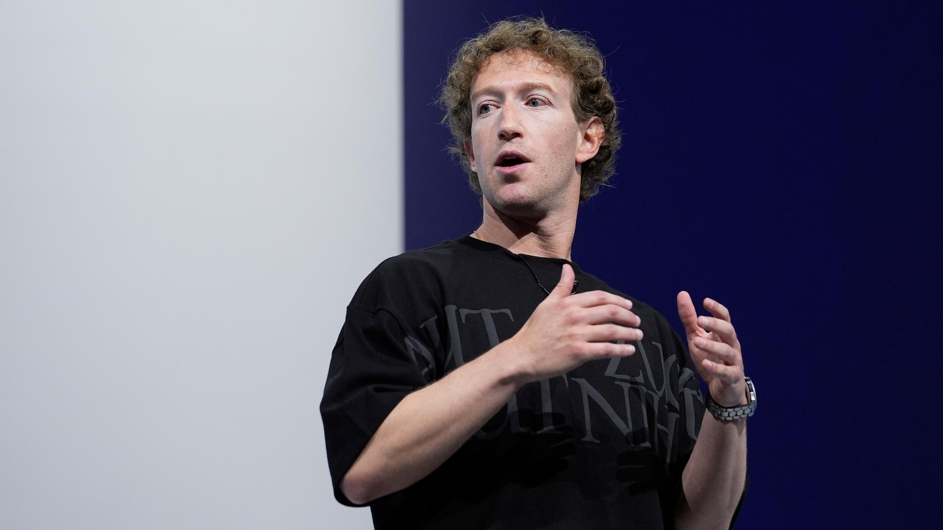 Meta-Chef Mark Zuckerberg steht vor einer schwarz-weißen Wand und spricht in ein Mikrofon. 