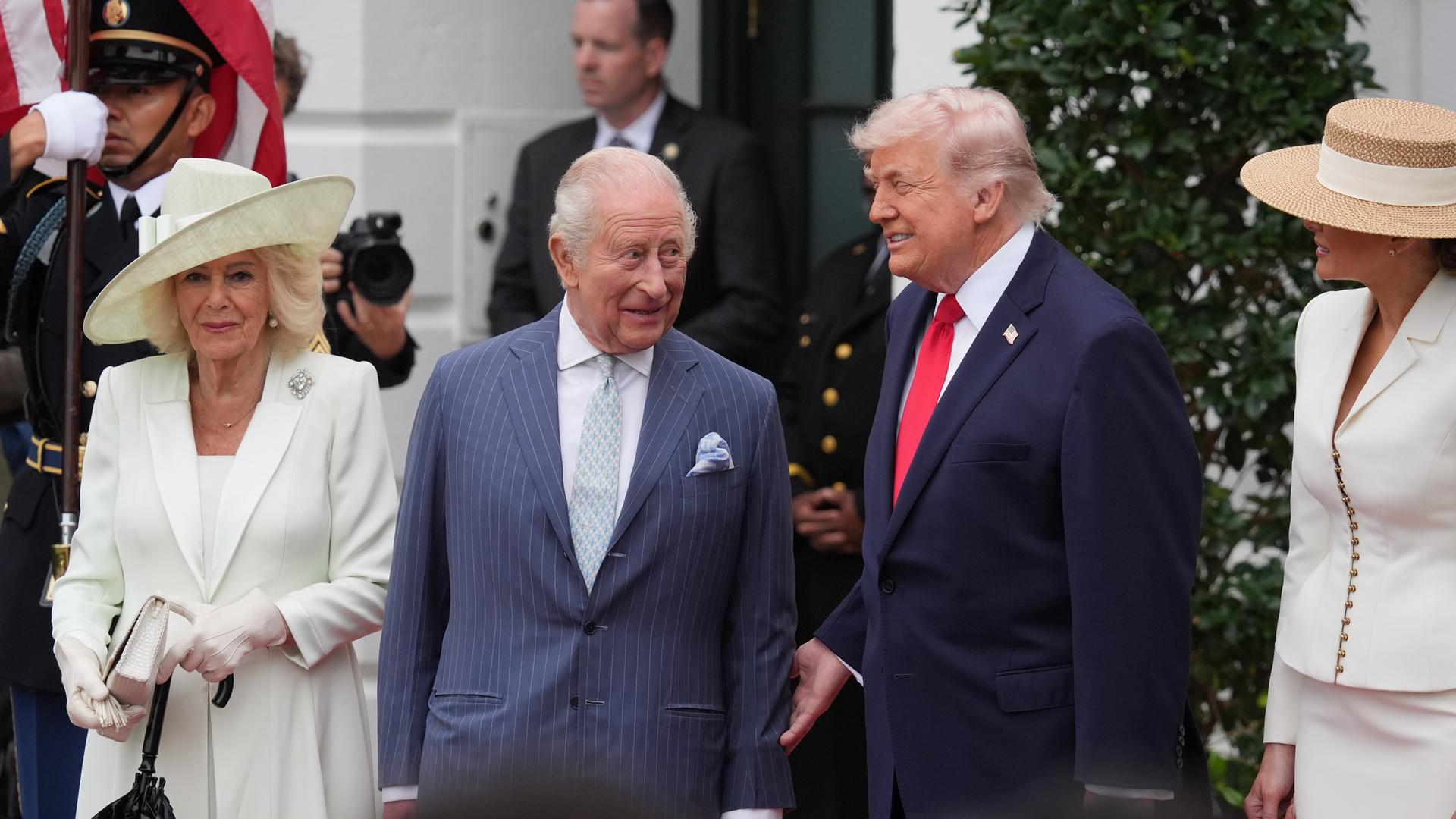 König Charles und US-Präsident Trump stehen vor dem Weißen Haus und reden miteinander. Neben Charles steht Camilla, in einem weißen Kleid und mit einem großen weißen Hut.