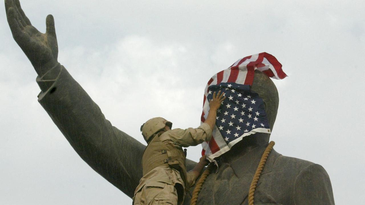 Das Foto zeigt einen US-Soldaten, der am 9. April 2003 das Gesicht der Statue des irakischen Präsidenten Saddam Hussein mit der US-Flagge auf dem al-Fardous-Platz in Bagdad bedeckt.