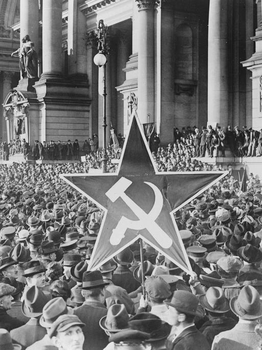 Demonstrierende vor dem Berliner Reichstag halten einen Stern mit Hammer und Sichel in die Höhe.