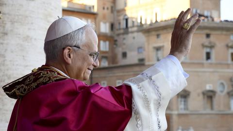 Leo XIV winkt lächelnd vom Balkon des Petersdoms. Er ist von der Seite fotografiert.