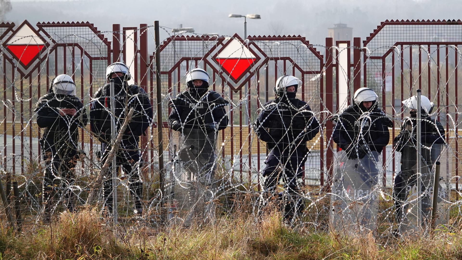 Polnische Sicherheitskräfte stehen an der Grenze zu Belarus hinter Stacheldraht.