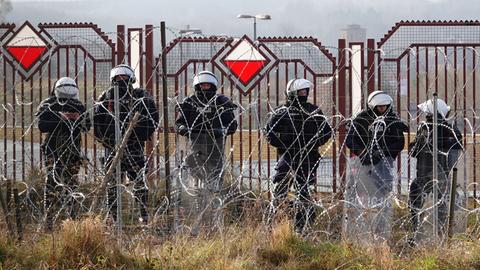 Polnische Sicherheitskräfte stehen an der Grenze zu Belarus hinter Stacheldraht.
