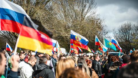 Auf einer Demonstration stehen hunderte Menschen zwischen vielen russischen und einer vereinzelten deutschen Flagge