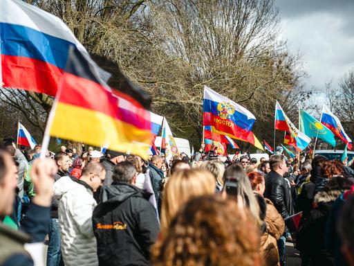 Auf einer Demonstration stehen hunderte Menschen zwischen vielen russischen und einer vereinzelten deutschen Flagge