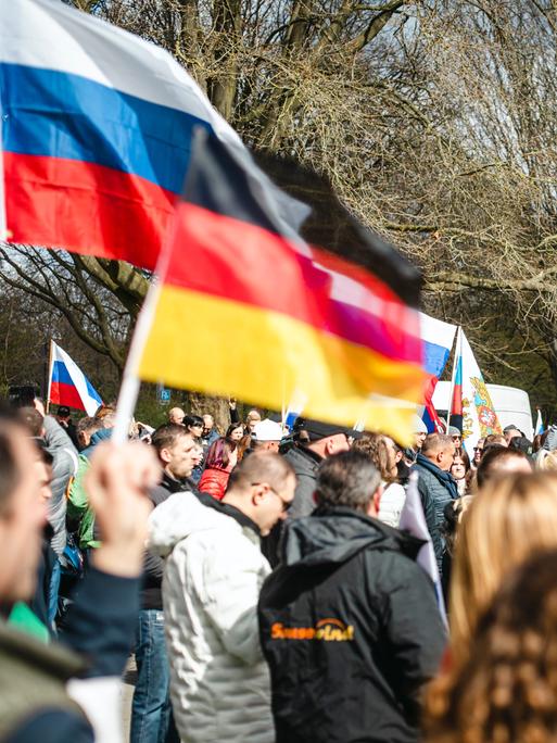 Auf einer Demonstration stehen hunderte Menschen zwischen vielen russischen und einer vereinzelten deutschen Flagge