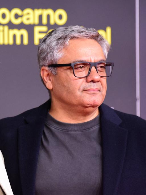 Jafar Panahi und Mohammad Rasoulof stehen nebeneinander vor einer Wand auf der "Locarno Filmfestival" steht. 