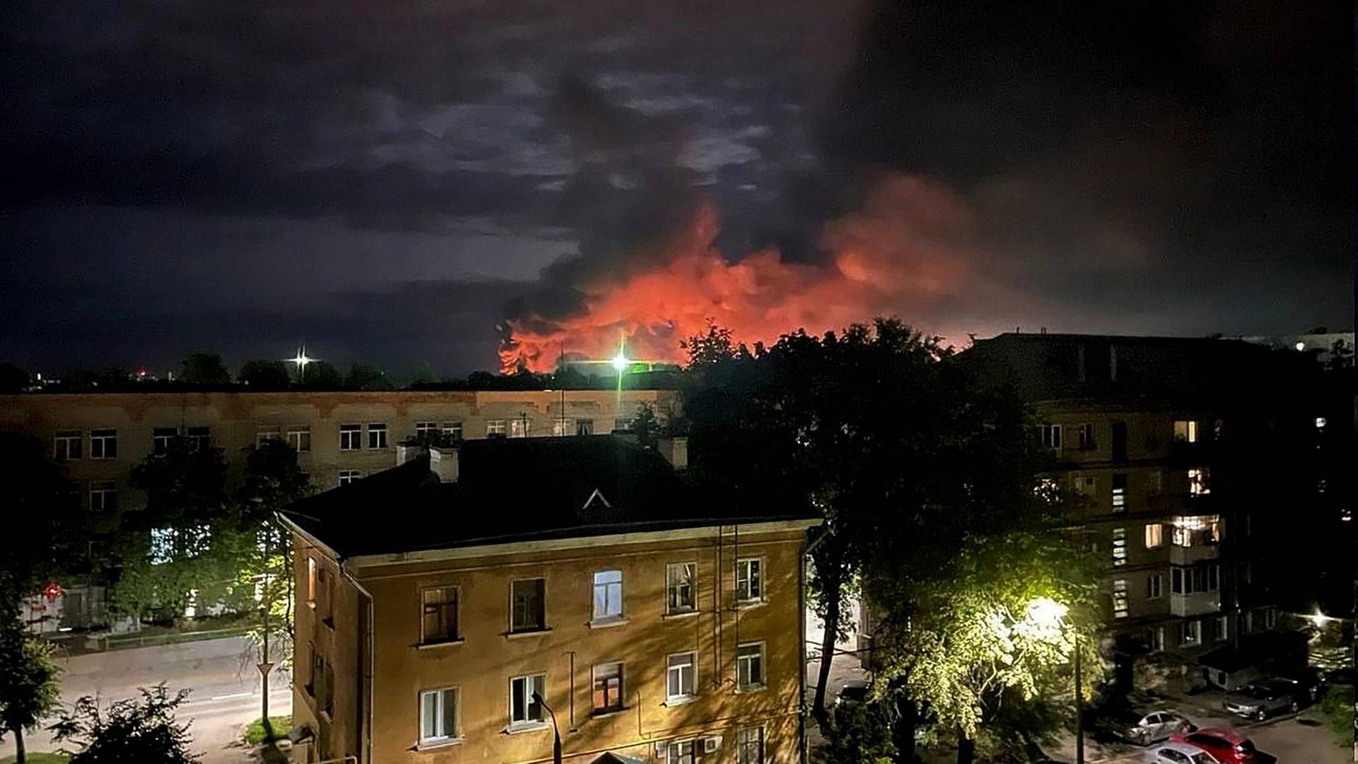 Rauch mit steigt im Hintergrund über der Region Pskov in Russland auf. Im Vordergrund ein hell beleuchtetes Wohnhaus.
