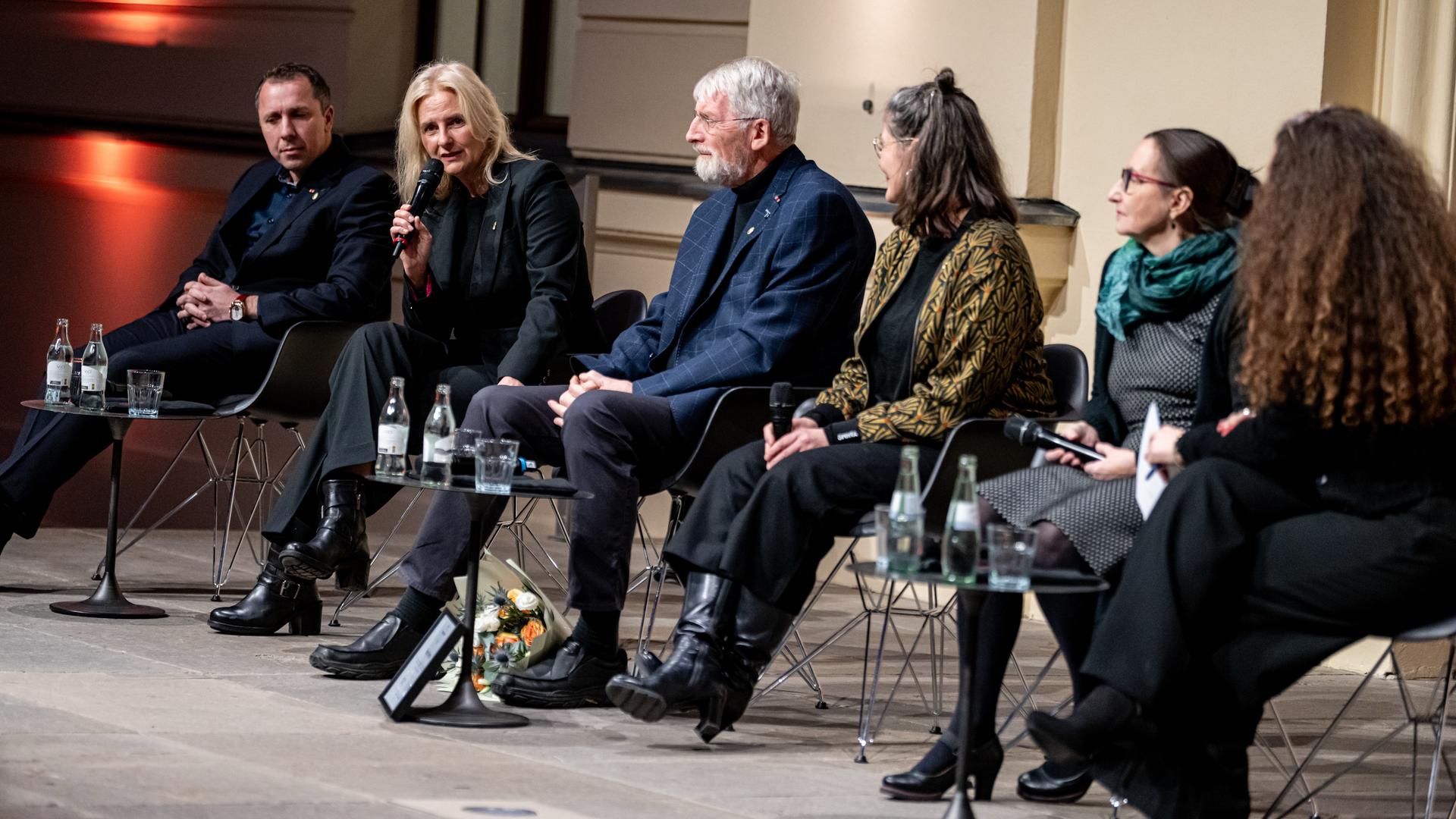 Preisträgerinnen und Preisträger sitzen bei der Verleihung der Obermayer-Awards nebeneinander auf Stühlen auf einer Bühne. Eine von ihnen hält ein Mikrofon in der Hand und spricht hinein.