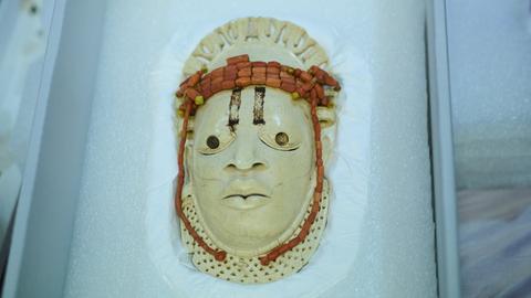 Eine Maske aus Elfenbein liegt gebettet auf einem weissen Kissen.