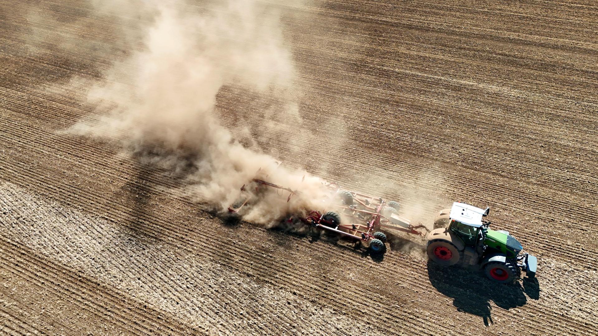 Ein Traktor zieht ein landwirtschaftliches Gerät ueber ein extrem trockenes Feld und wirbelt dabei eine riesige Staubwolke auf. Ein Traktor zieht ein landwirtschaftliches Gerät ueber ein extrem trockenes Feld und wirbelt dabei eine riesige Staubwolke auf.