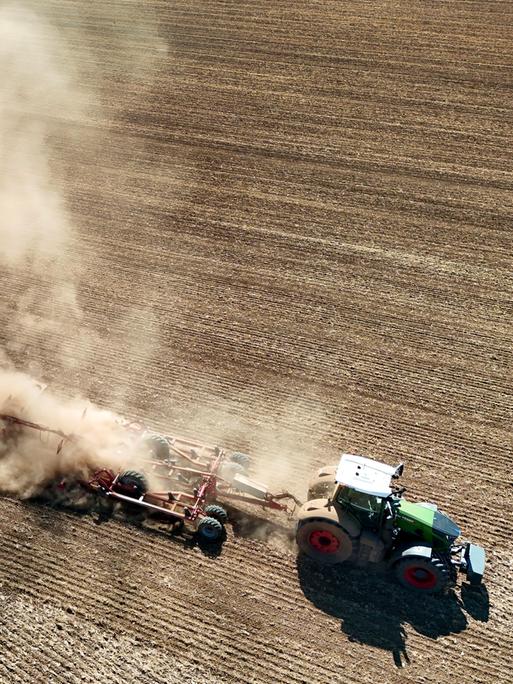 Ein Traktor zieht ein landwirtschaftliches Gerät ueber ein extrem trockenes Feld und wirbelt dabei eine riesige Staubwolke auf. Ein Traktor zieht ein landwirtschaftliches Gerät ueber ein extrem trockenes Feld und wirbelt dabei eine riesige Staubwolke auf.