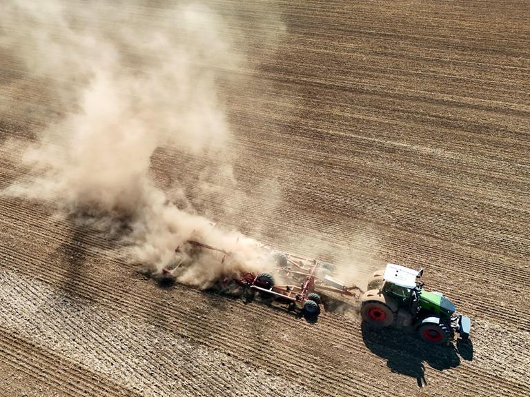 Ein Traktor zieht ein landwirtschaftliches Gerät ueber ein extrem trockenes Feld und wirbelt dabei eine riesige Staubwolke auf. Ein Traktor zieht ein landwirtschaftliches Gerät ueber ein extrem trockenes Feld und wirbelt dabei eine riesige Staubwolke auf.