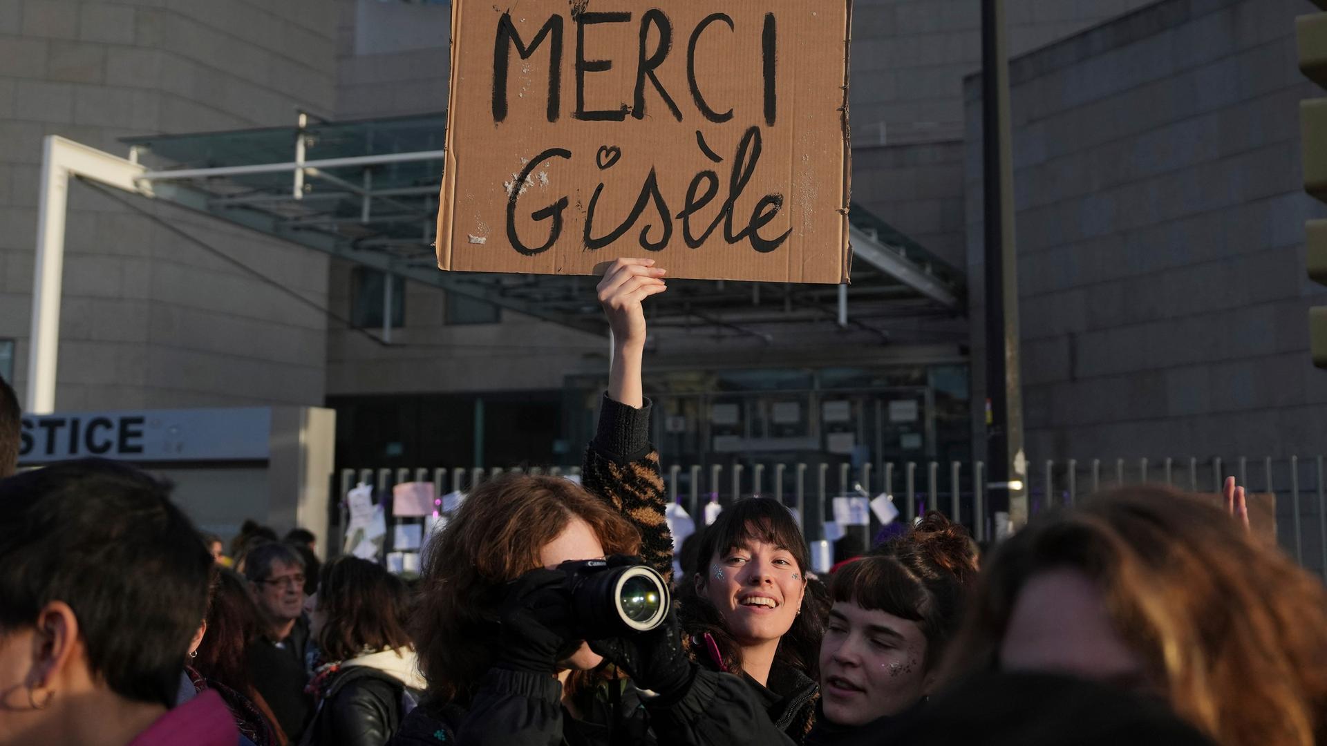 Eine Frau hält ein Plakat mit dem Schriftzug "Merci Gisèle" in die Höhe. 