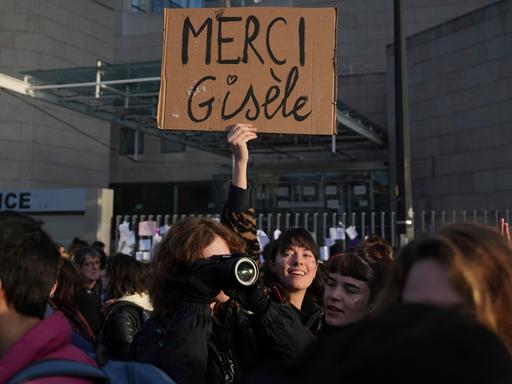 Eine Frau hält ein Plakat mit dem Schriftzug "Merci Gisèle" in die Höhe. 