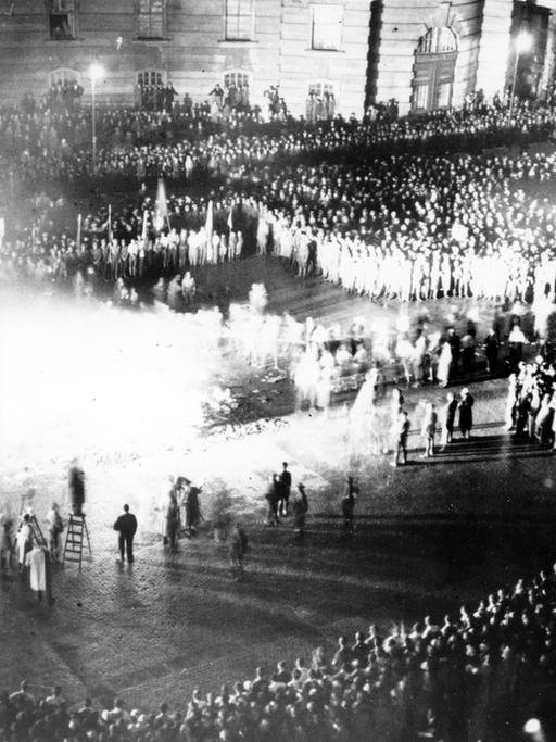 Historisches Schwarzweißfoto einer großen Menschenmenge, die um einen brennenden Scheiterhaufen herumsteht.