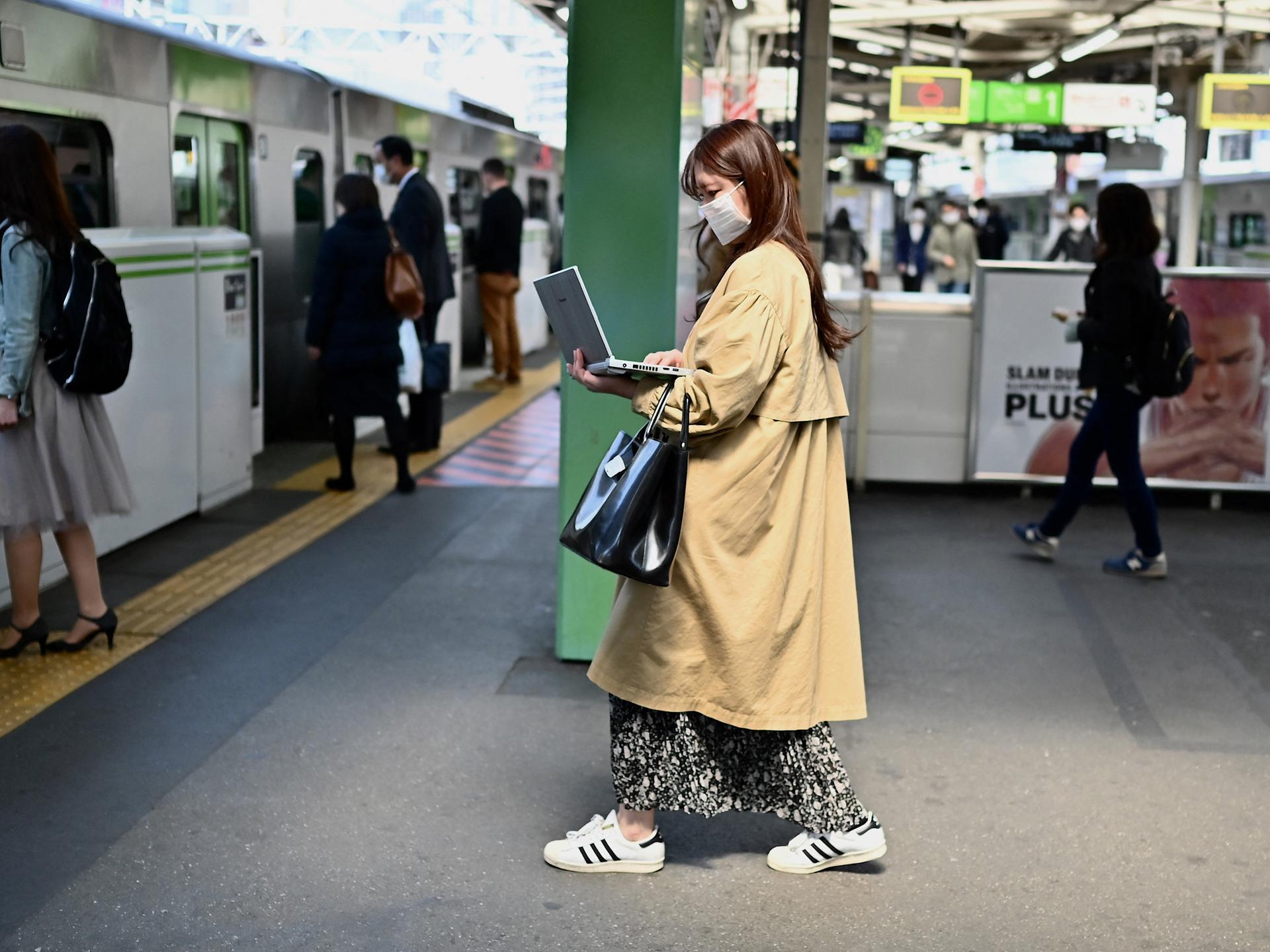 Eine Frau arbeitet im Stehen an ihrem Laptop, während sie am Bahnhof Gotanda in Tokio in einen Zug einsteigt.