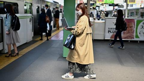 Eine Frau arbeitet im Stehen an ihrem Laptop, während sie am Bahnhof Gotanda in Tokio in einen Zug einsteigt.