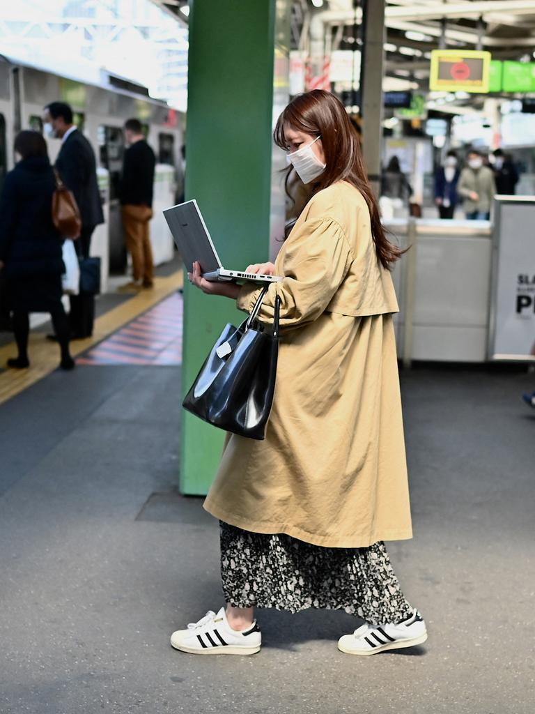 Eine Frau arbeitet im Stehen an ihrem Laptop, während sie am Bahnhof Gotanda in Tokio in einen Zug einsteigt.