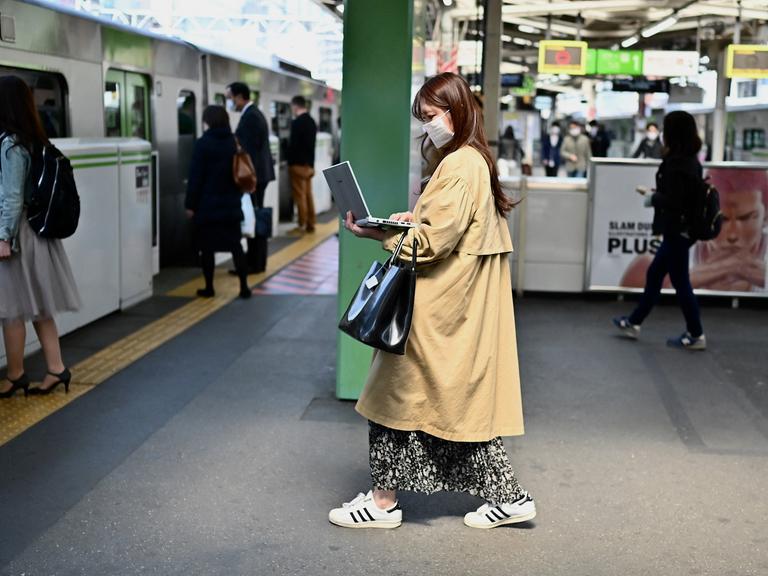 Eine Frau arbeitet im Stehen an ihrem Laptop, während sie am Bahnhof Gotanda in Tokio in einen Zug einsteigt.