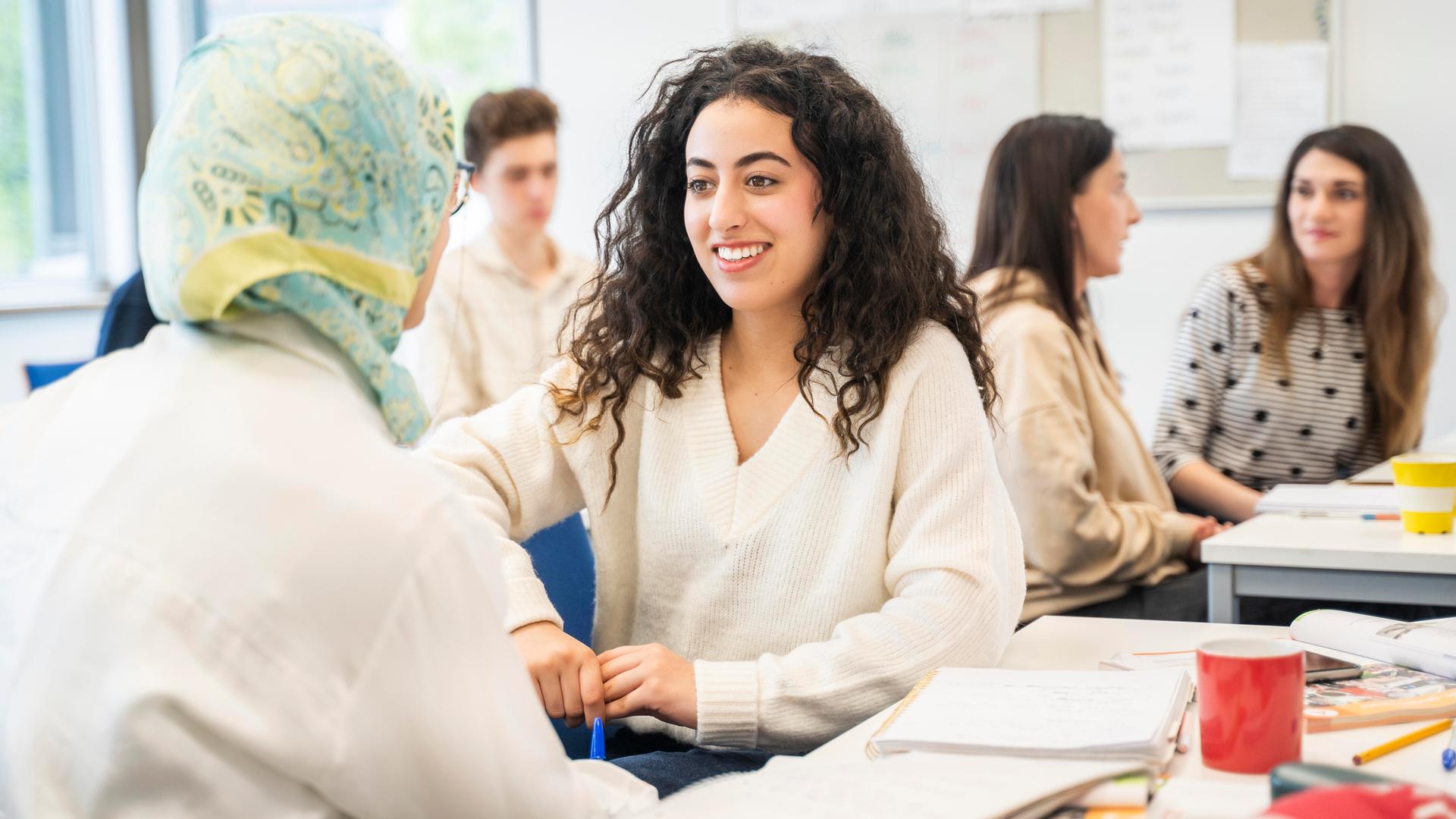 Schülerinnen und Schüler unterschiedlicher Herkunft nehmen an einem Sprachkurs teil. Eine von ihnen trägt ein Kopftuch. (Symbolfoto)