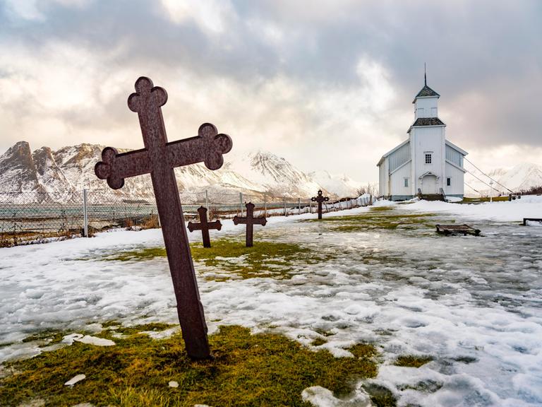 Gimsøy Kirche mit Friedhof, hinten schneebedeckte Berge, Winter, Gimsøya, Lofoten, Norwegen, Europa