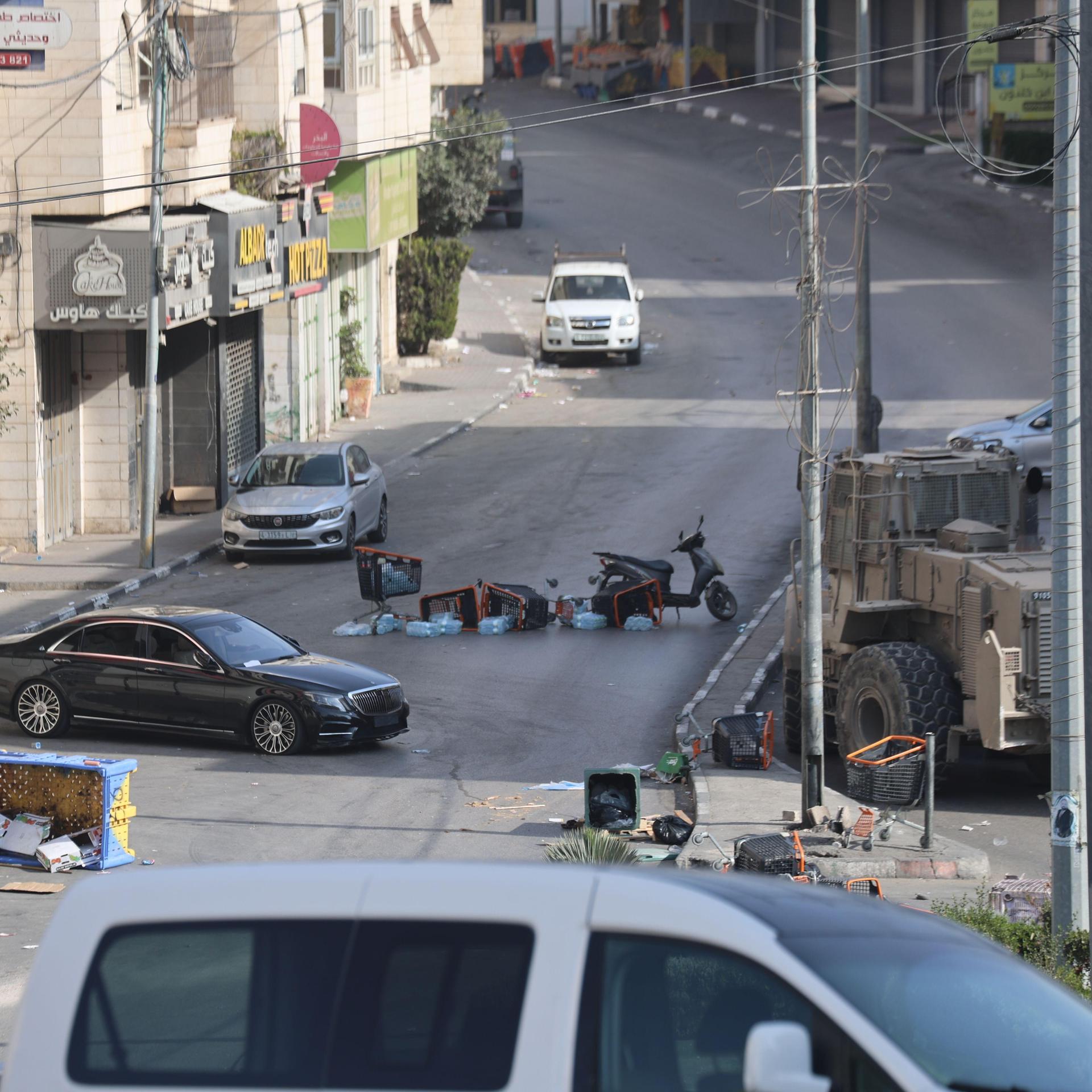 Kisten und ein Mopeds liegen umgekippt auf einer verlassenen Straße in Hebron.