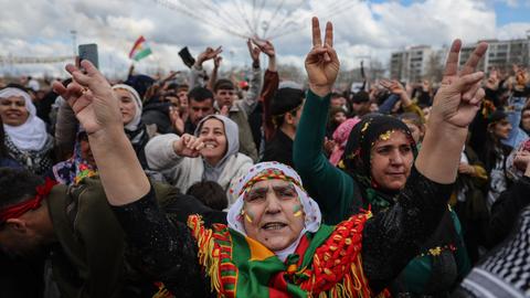 Menschen tanzen und singen während der Newroz-Feierlichkeiten auf einer Straße. Einige Frauen haben das Gesicht in den Farben der kurdischen Flagge (rot, weiß, grün und gelb) bemalt und zeigen mit ihren Händen das Victory-Zeichen. Menschen tanzen und singen während der Newroz-Feierlichkeiten auf einer Straße. Einige Frauen haben das Gesicht in den Farben der kurdischen Flagge (rot, weiß, grün und gelb) bemalt und zeigen mit ihren Händen das Victory-Zeichen.
