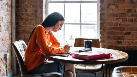 Eine junge Frau sitzt in einem Cafe und schreibt.