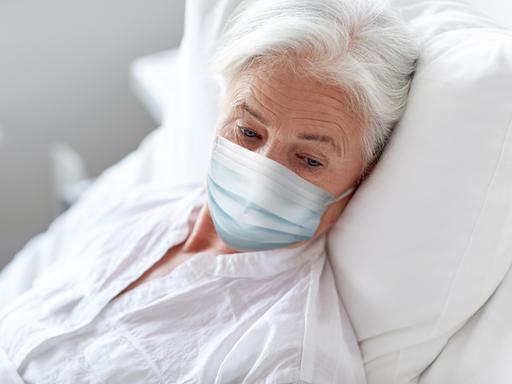 Eine Seniorin liegt mit Maske in einem Krankenbett.