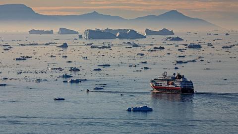 Ein Schiff bei Mitternachtssohnne vor Eisbergen