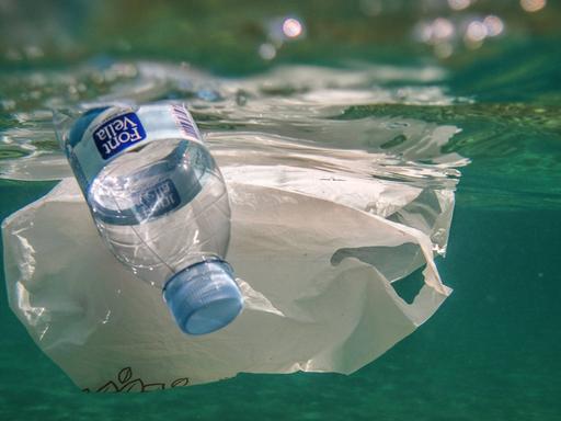 Unterwasseraufnahme zeigt Plastikflasche und Plastiktüte im Meer treibend.