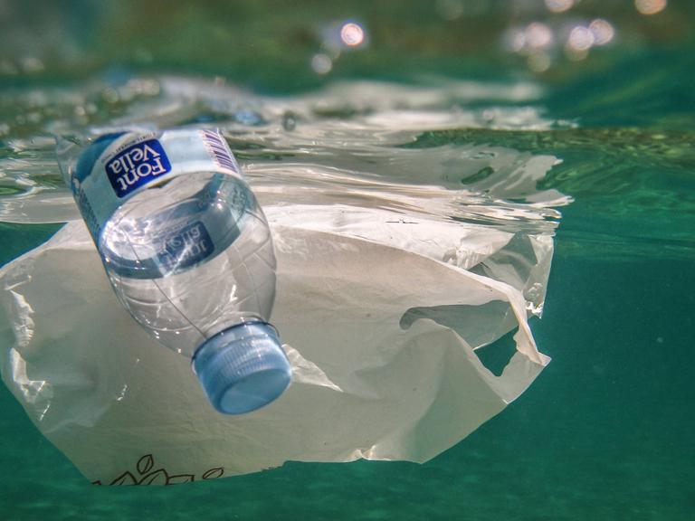 Unterwasseraufnahme zeigt Plastikflasche und Plastiktüte im Meer treibend.