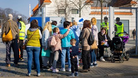 Familien mit Kindern stehen vor einem Zaun.