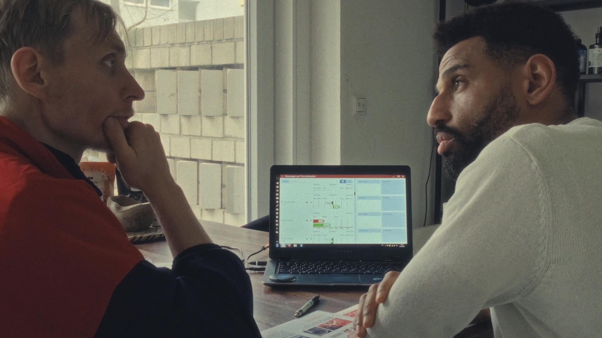Der Protagonist aus dem Film „Soldaten des Lichts“ David (rechts im Bild) ist mit einem Anhänger seiner sektenähnlichen Gruppe im Gespräch. Die beiden sitzen am Schreibtisch. Im Hintergrund leuchtet ein Laptop. Der Protagonist aus dem Film „Soldaten des Lichts“ David (rechts im Bild) ist mit einem Anhänger seiner sektenähnlichen Gruppe im Gespräch. Die beiden sitzen am Schreibtisch. Im Hintergrund leuchtet ein Laptop.