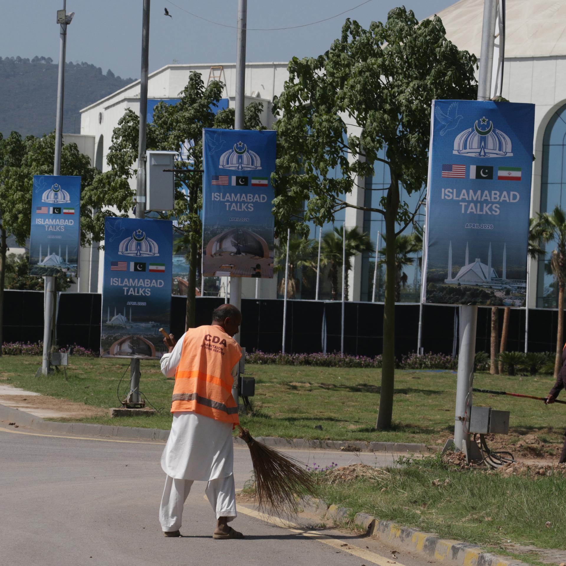 Ein Arbeiter reinigt am 19. April 2026 in Islamabad eine Straße neben Plakaten zu den US-Iran-Gesprächen im Vorfeld der zweiten Verhandlungsrunde.