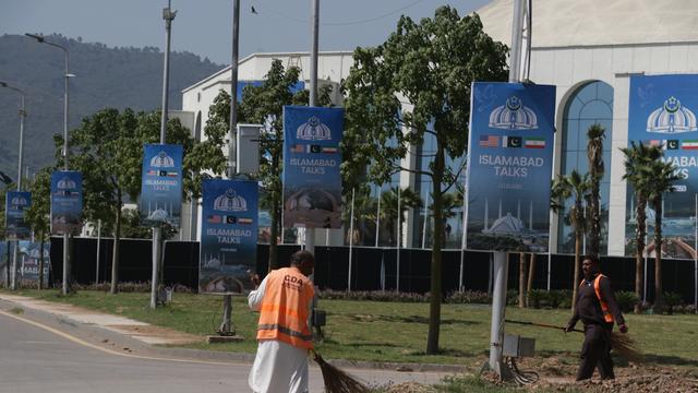Ein Arbeiter reinigt am 19. April 2026 in Islamabad eine Straße neben Plakaten zu den US-Iran-Gesprächen im Vorfeld der zweiten Verhandlungsrunde.