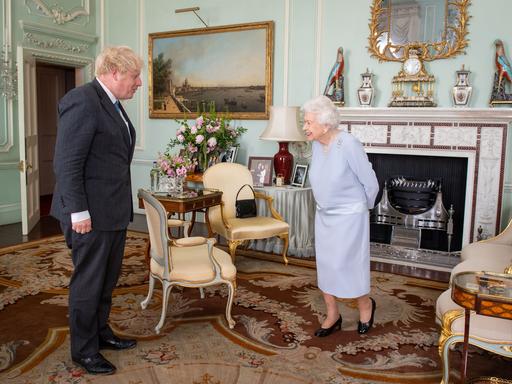 Boris Johnson und die Queen stehen sich gegenüber und sprechen miteinander.