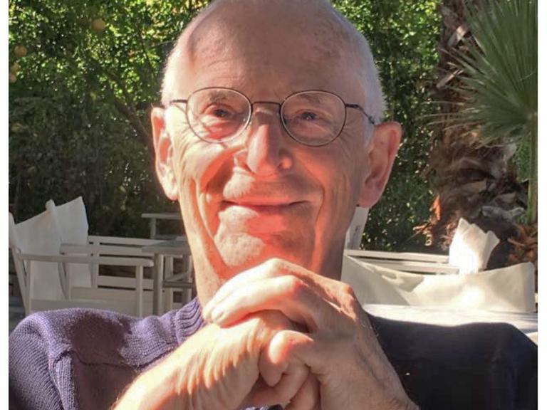 Klaus Hinrich Stahmer blickt in einer Gartenumgebung freundlich in die Kamera, während er seine Hände vor dem Kinn gefaltet hat. 