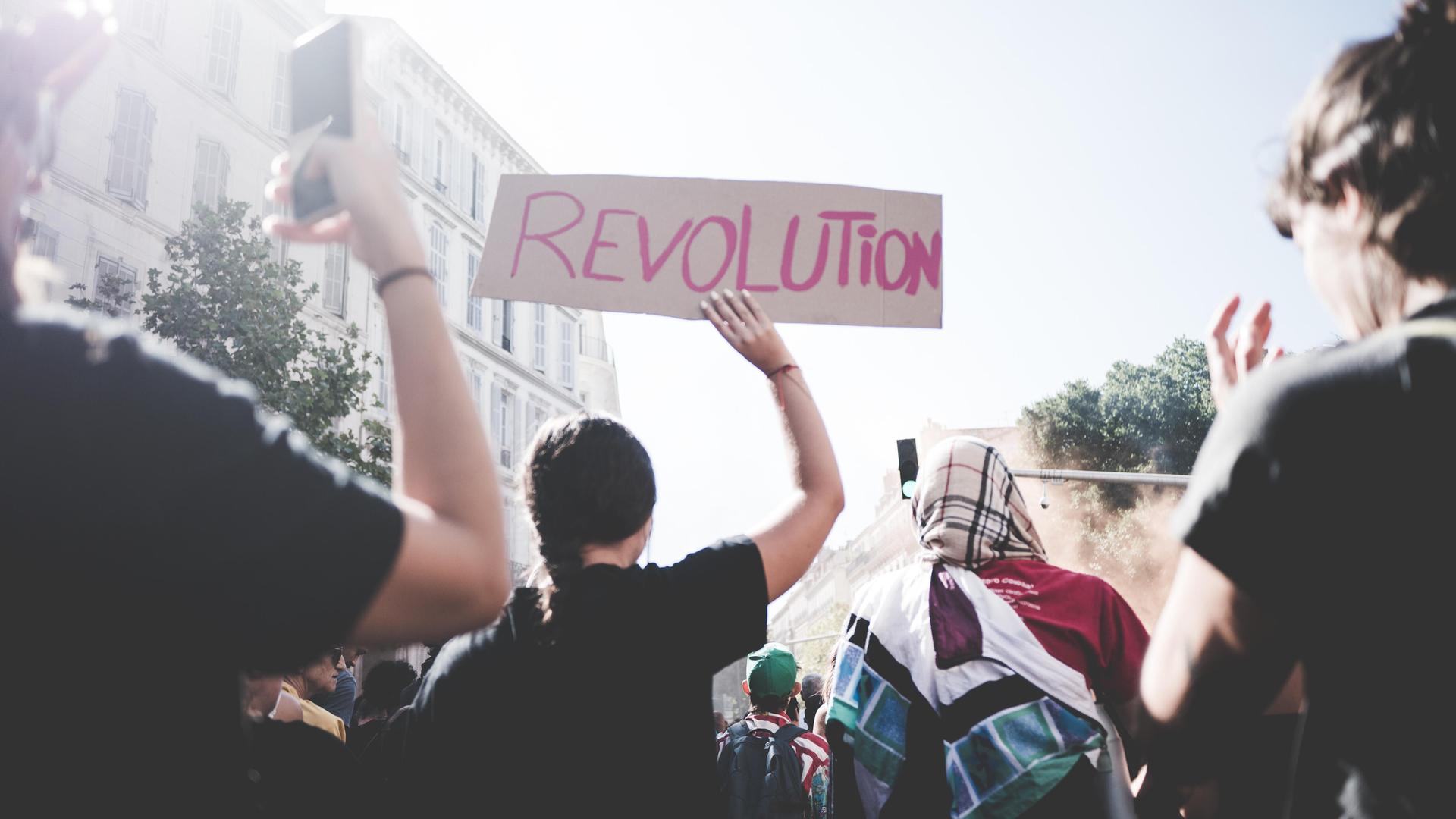 EIne Demonstrantin hält ein Schild mit der Aufschrift "Revolution" in die Höhe