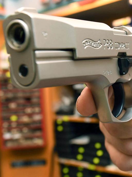 Ein Verkäufer hält in einem Waffengeschäft eine Pistole in der Hand. 