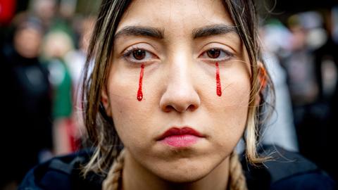 Portrait einer Frau, der rote Tränen die wie Blut anmuten, die Wangen herabfließen