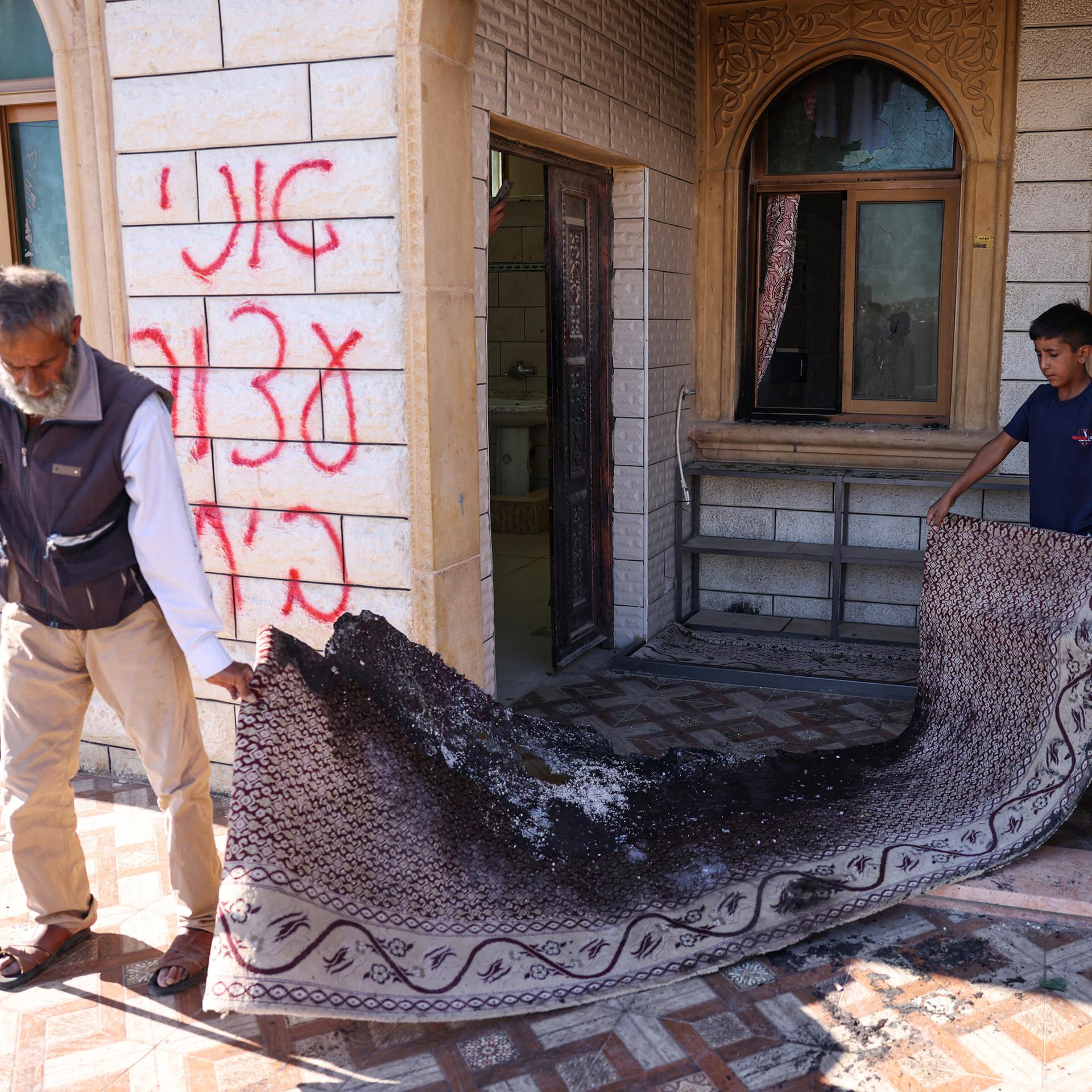 Ein palästinensischer Mann und ein Kind tragen einen verbrannten Teppich aus einer Moschee, deren Eingang in Brand gesetzt wurde. 