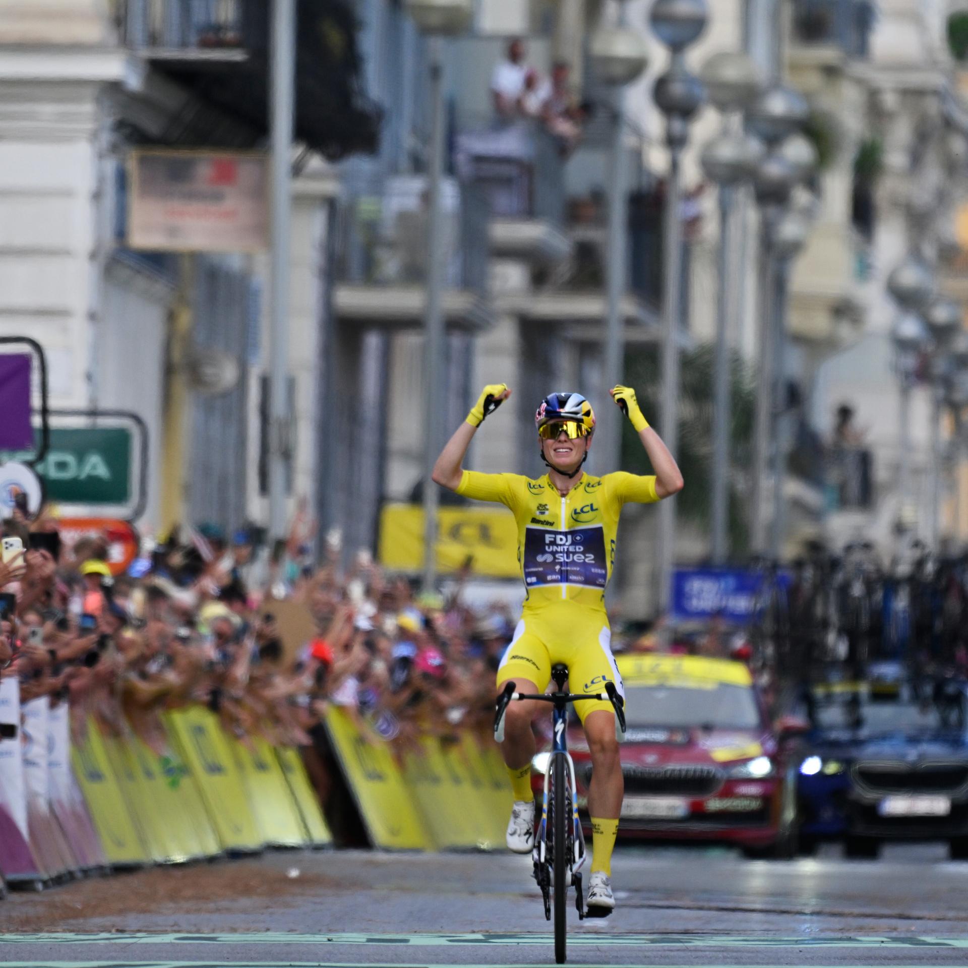 Demi Vollering feiert auf der Ziellinie ihren Sieg bei der Tour. Sie trägt das gelbe Trikot und hat die Arme nach oben gereckt.